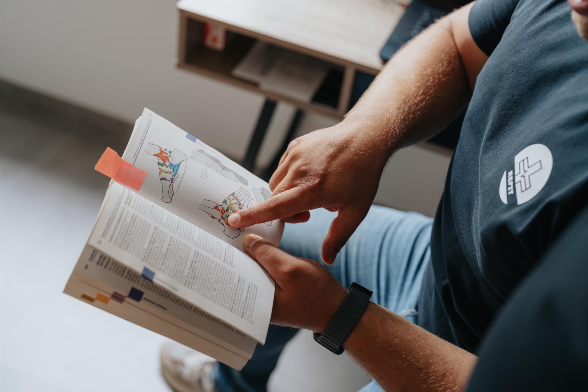 Intake voor shockwave therapie in Pelt: kinesitherapeut van Refit licht een klacht toe met een anatomieboek
